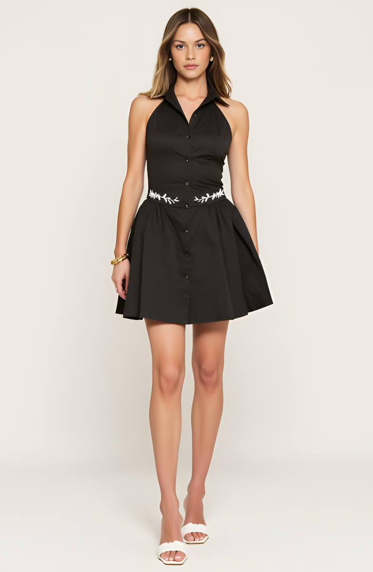 Woman in a black halter neck dress with white embroidery and white heels