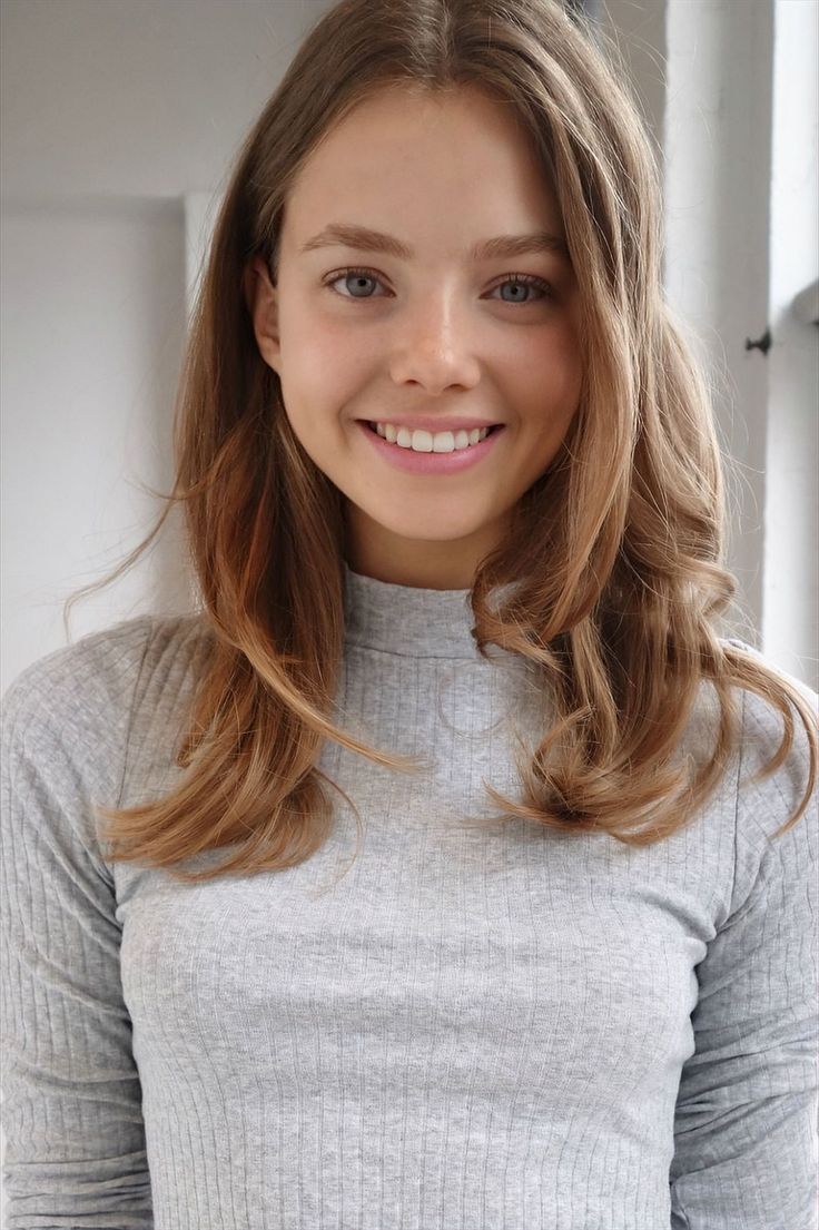 Young woman with long hair and a grey ribbed top smiling at the camera