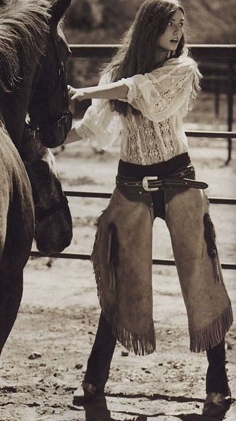 Woman in cowboy chaps and a lace shirt with a horse in a sepia-toned photograph