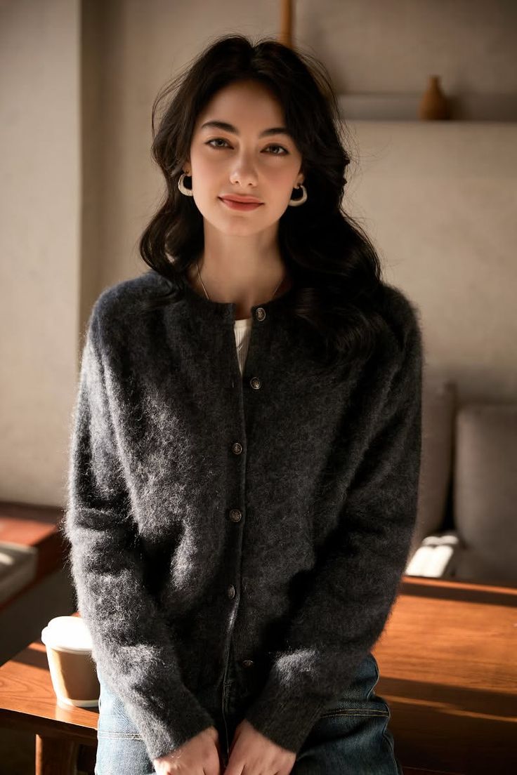 Woman with long dark hair wearing a cardigan and jeans indoors