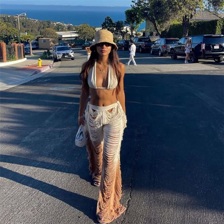 Woman in a bikini top and ripped pants walking on a street with ocean view