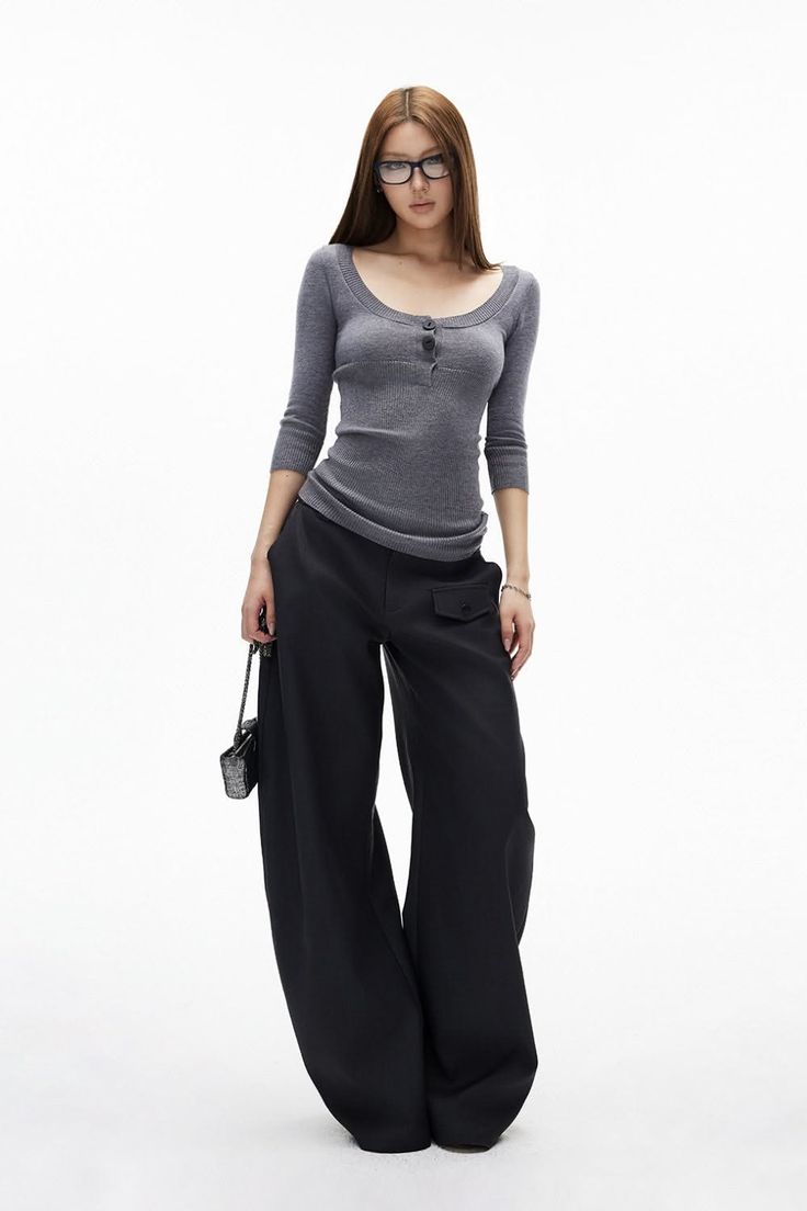 Woman with long hair and glasses wearing a gray top and wide leg pants
