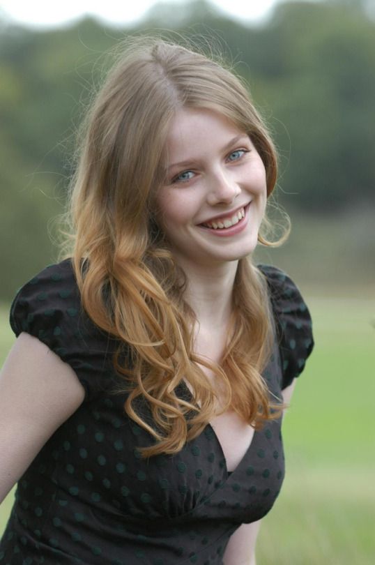 Smiling woman with long blonde hair in a black polka dot dress outdoors