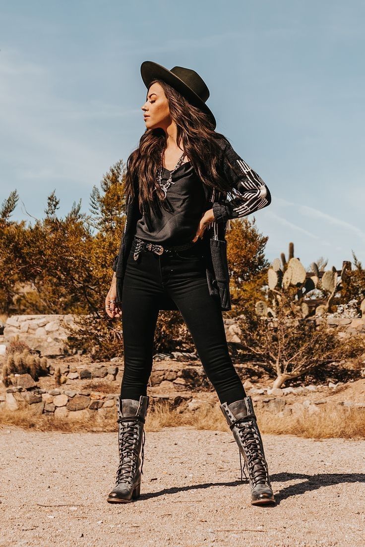 Woman in a cowboy hat and black jeans posing in a desert landscape