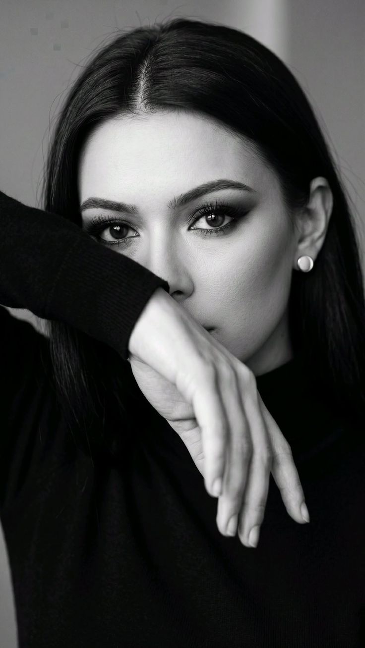 Woman with dark hair and dramatic eye makeup covering her mouth with her arm