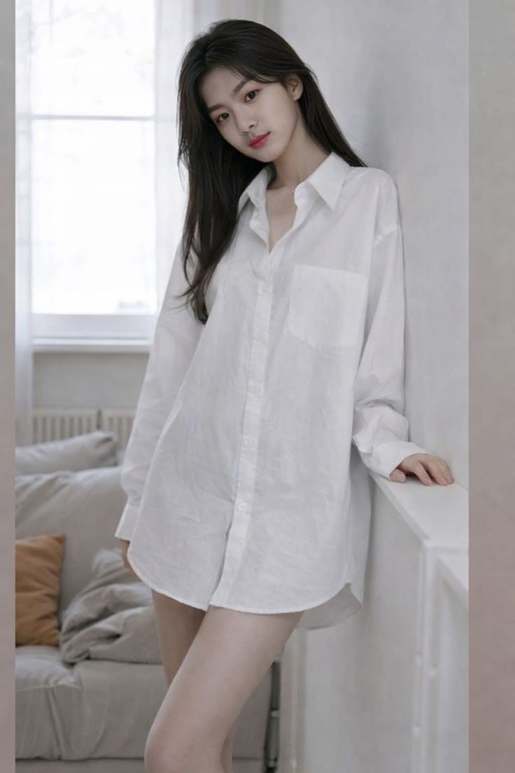 Woman in an oversized white shirt leaning against a wall indoors