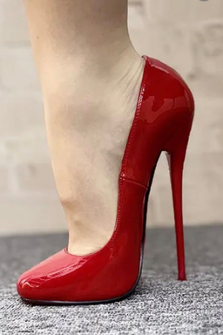 Foot in a red patent leather stiletto high heel shoe on a grey carpet