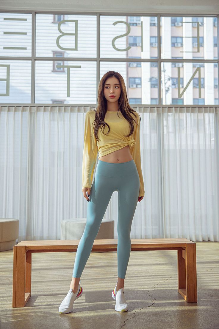 Woman in a yellow crop top and blue leggings standing indoors