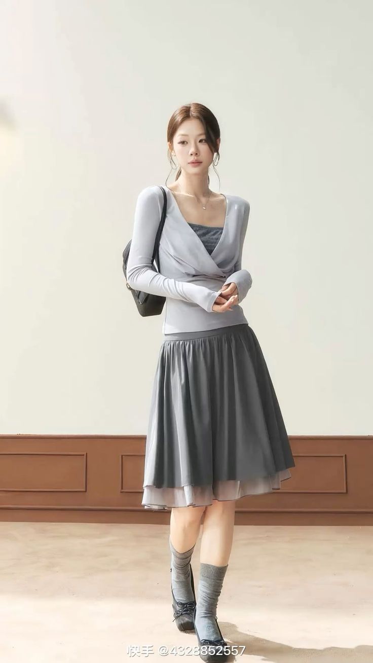Woman in a light gray long sleeve top and a dark gray midi skirt indoors