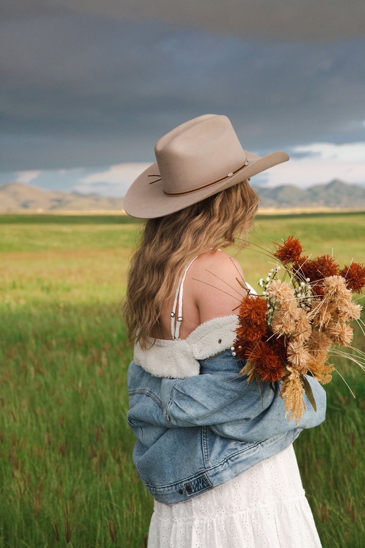 Woman in a cowboy hat and denim jacket holding a bouquet in a green field
