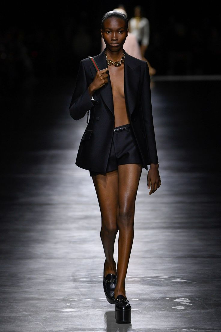 Model in a black blazer and shorts with a choker on a dark runway