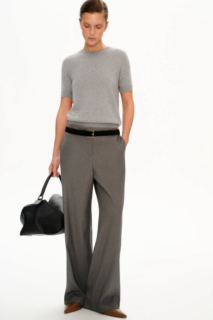 Woman in a gray t-shirt and wide leg pants holding a black handbag