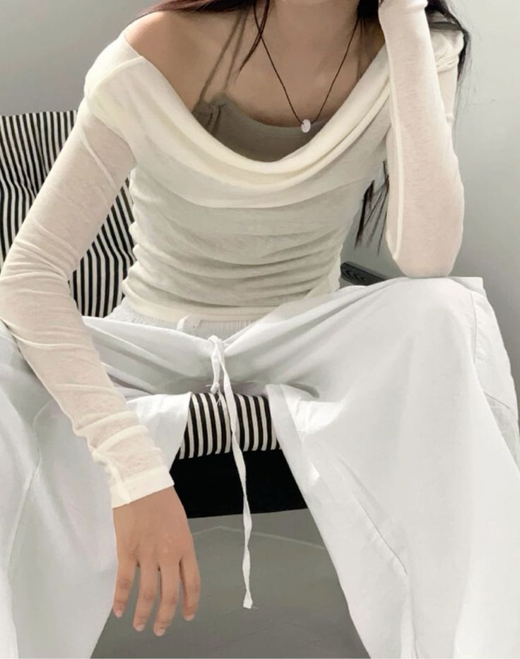 Person wearing an off-shoulder long-sleeve top and white pants indoors