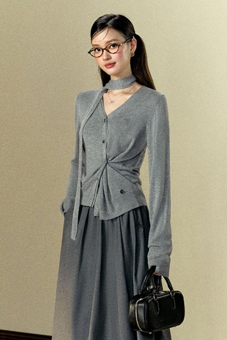 Woman in a gray cardigan and midi skirt holding a black handbag