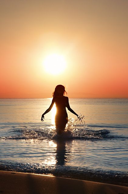 Woman silhouetted against a sunset, walking in the ocean with water splashing