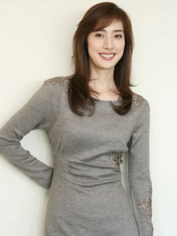 Woman with long brown hair wearing a gray dress with embroidered details, smiling