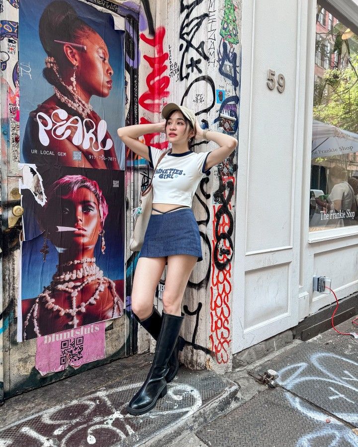Woman in a crop top and denim skirt posing against a graffiti-covered wall