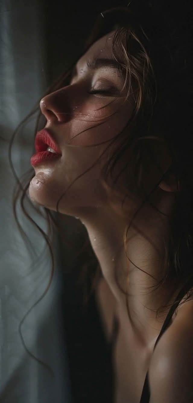 Woman with wet hair and red lipstick, eyes closed, in dramatic lighting