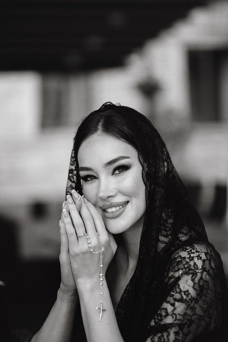 Woman in a lace veil holding a rosary with hands clasped in prayer
