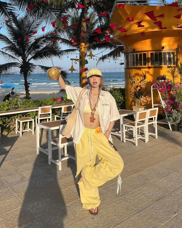 Woman in a yellow outfit holding a coconut drink on a sunny beach patio