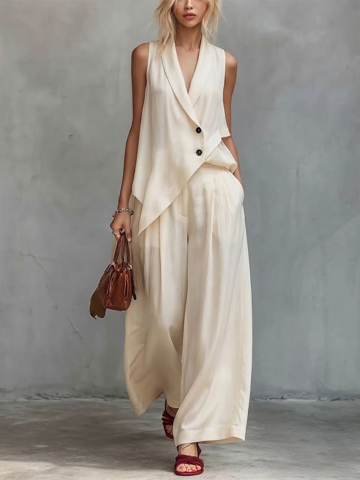 Woman in a cream sleeveless top and wide leg pants holding a brown handbag