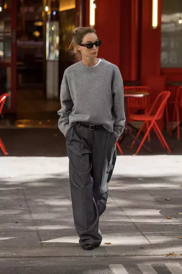 Woman in a grey sweater and wide leg pants walking on a street