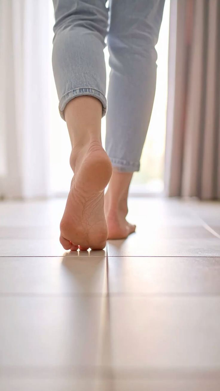 Person in jeans walking barefoot on a tiled floor indoors