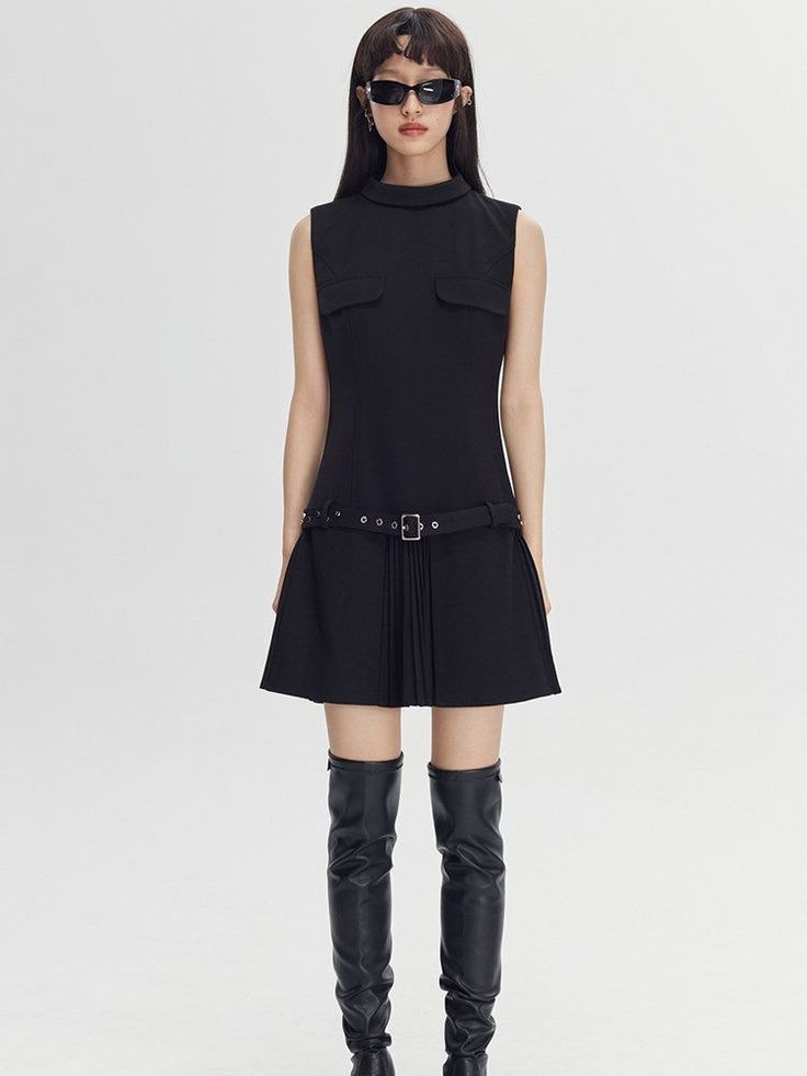 Woman in a black dress, sunglasses, and thigh-high boots in a studio setting