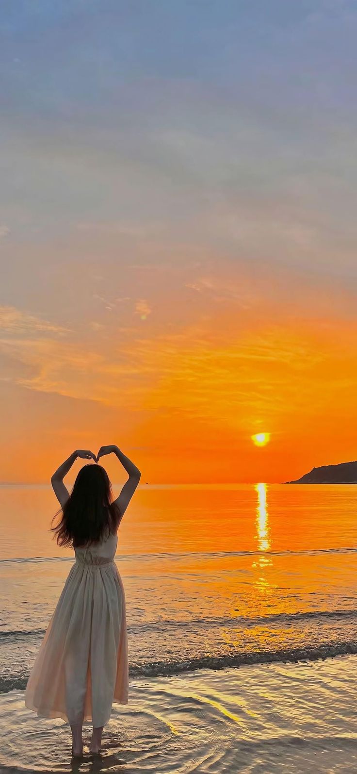 Woman making a heart shape with her hands at sunset on a beach