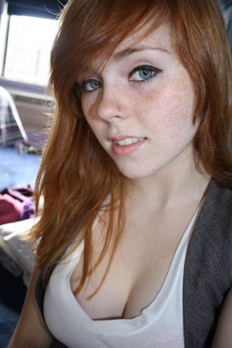Young woman with red hair and freckles wearing a white top indoors