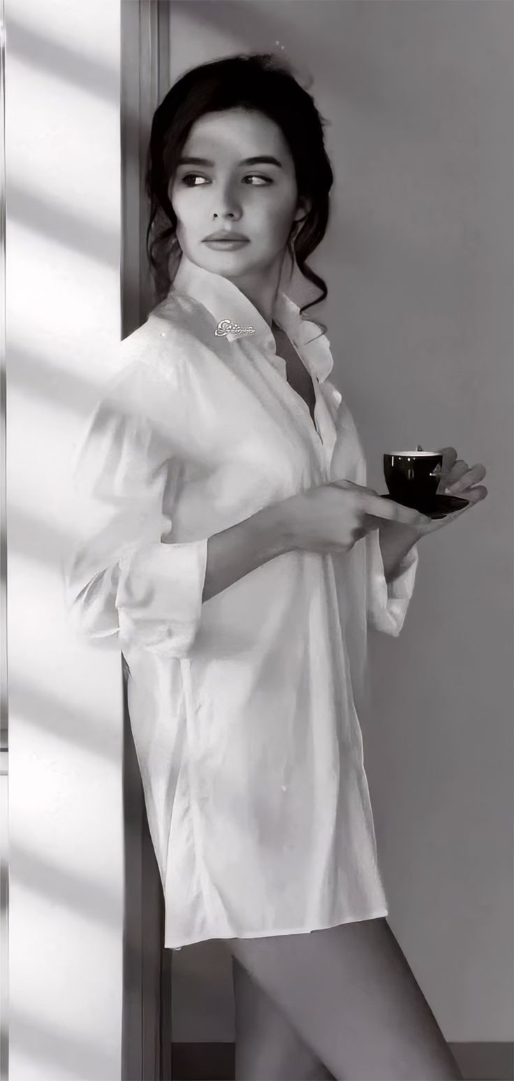 Woman in a white shirt holding a cup, with soft lighting and exposed skin