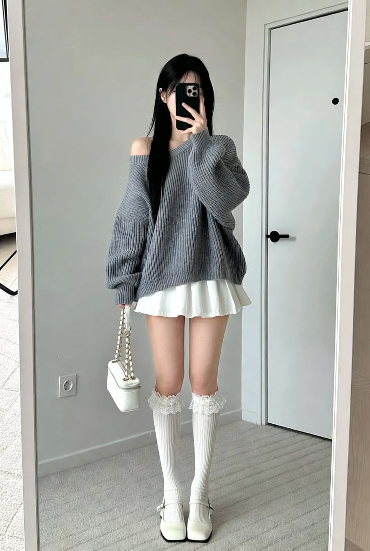Woman in an off-shoulder sweater and pleated skirt taking a mirror selfie