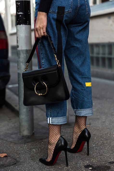 Person in blue jeans, fishnet stockings, and high heels holding a black handbag