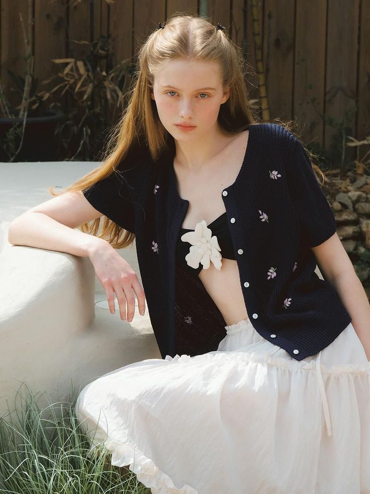 Young woman with long hair wearing a black cardigan and white skirt outdoors