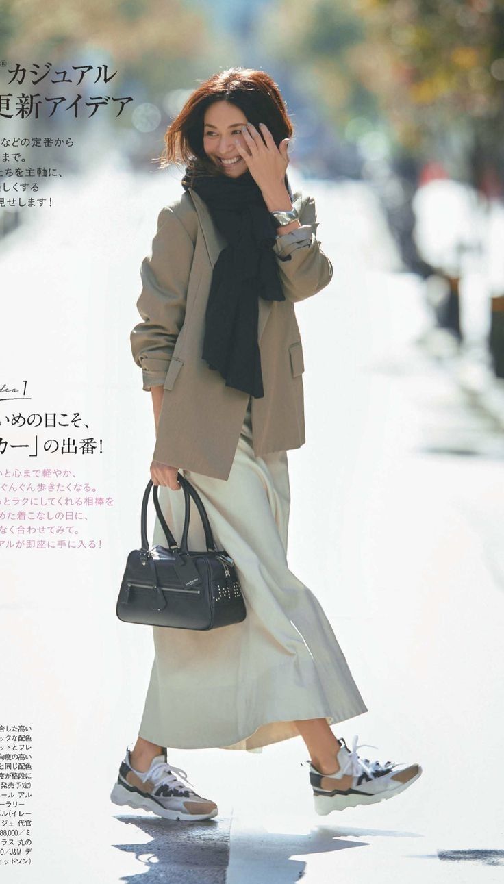 Woman in a blazer, scarf, and long skirt walking outdoors and smiling