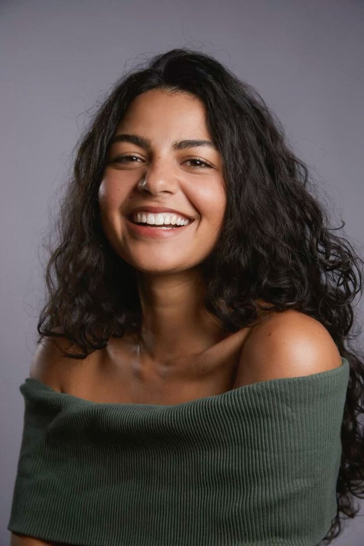 Woman with long dark hair wearing an off-shoulder green top, smiling at the camera