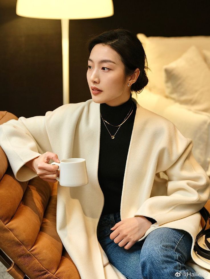 Woman in a white coat and black turtleneck holding a mug indoors
