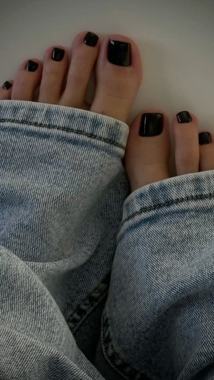 Feet with black nail polish peeking out from light wash denim jeans