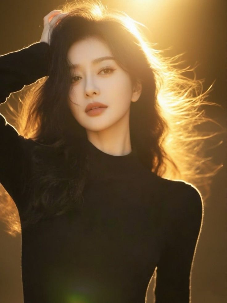 Woman with long black hair in a black top, backlit by golden hour light