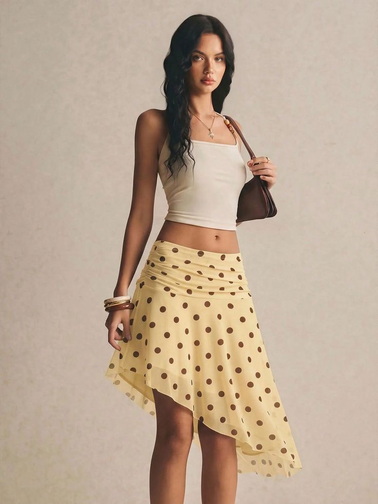 Woman in a white crop top and yellow polka dot skirt holding a brown handbag