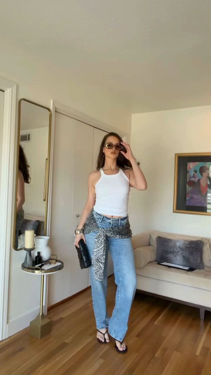 Woman in a white tank top and blue jeans posing indoors