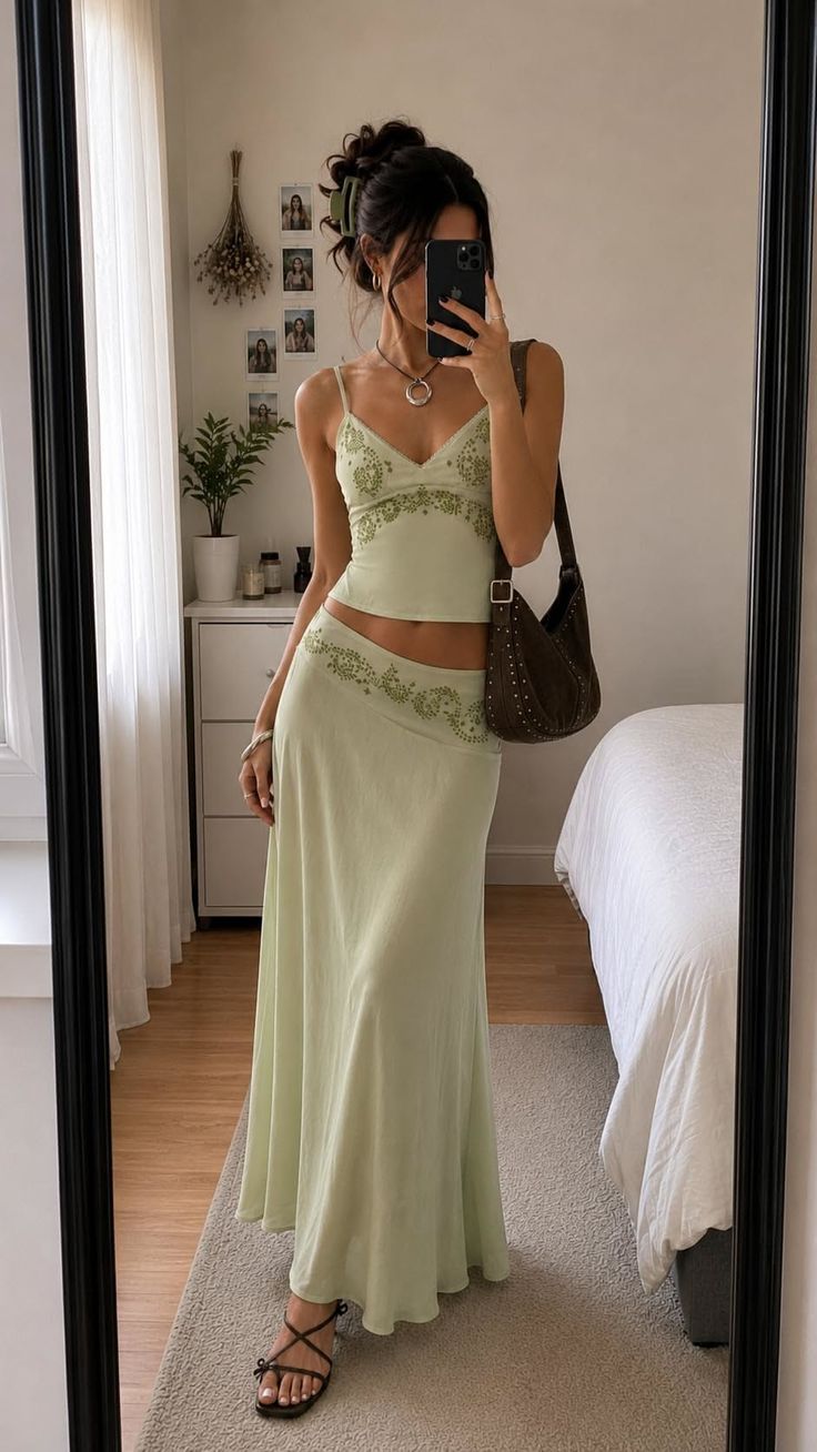 Woman in a light green two-piece outfit taking a mirror selfie indoors