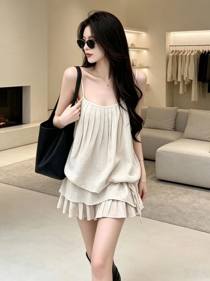 Woman with long black hair and sunglasses wearing a pleated top and mini skirt indoors