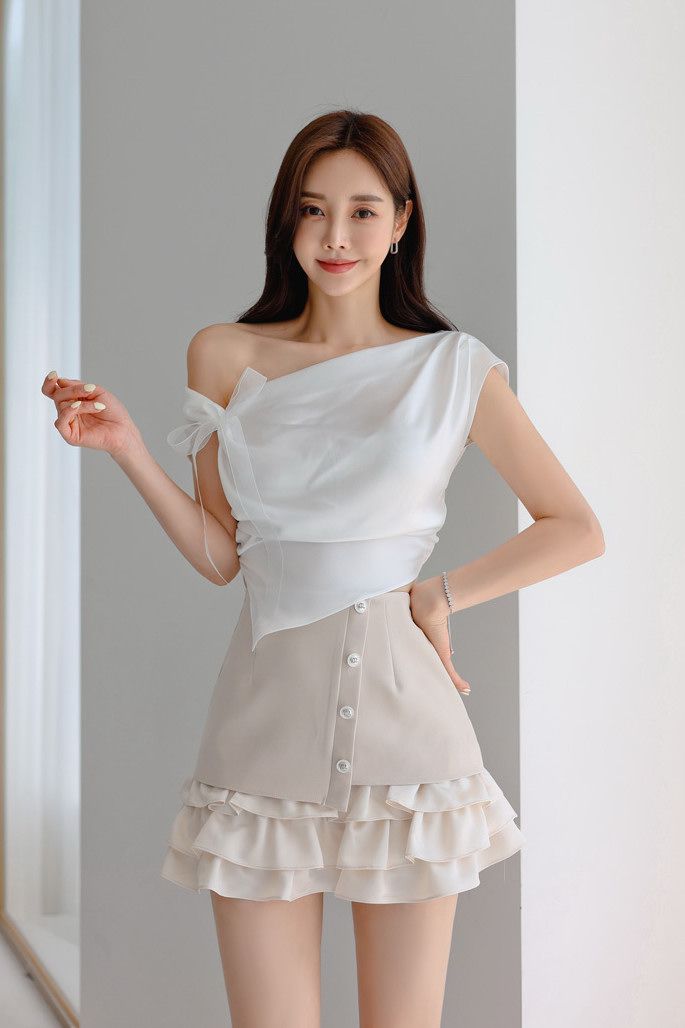 Woman with long hair wearing a white off-shoulder top and a ruffle mini skirt
