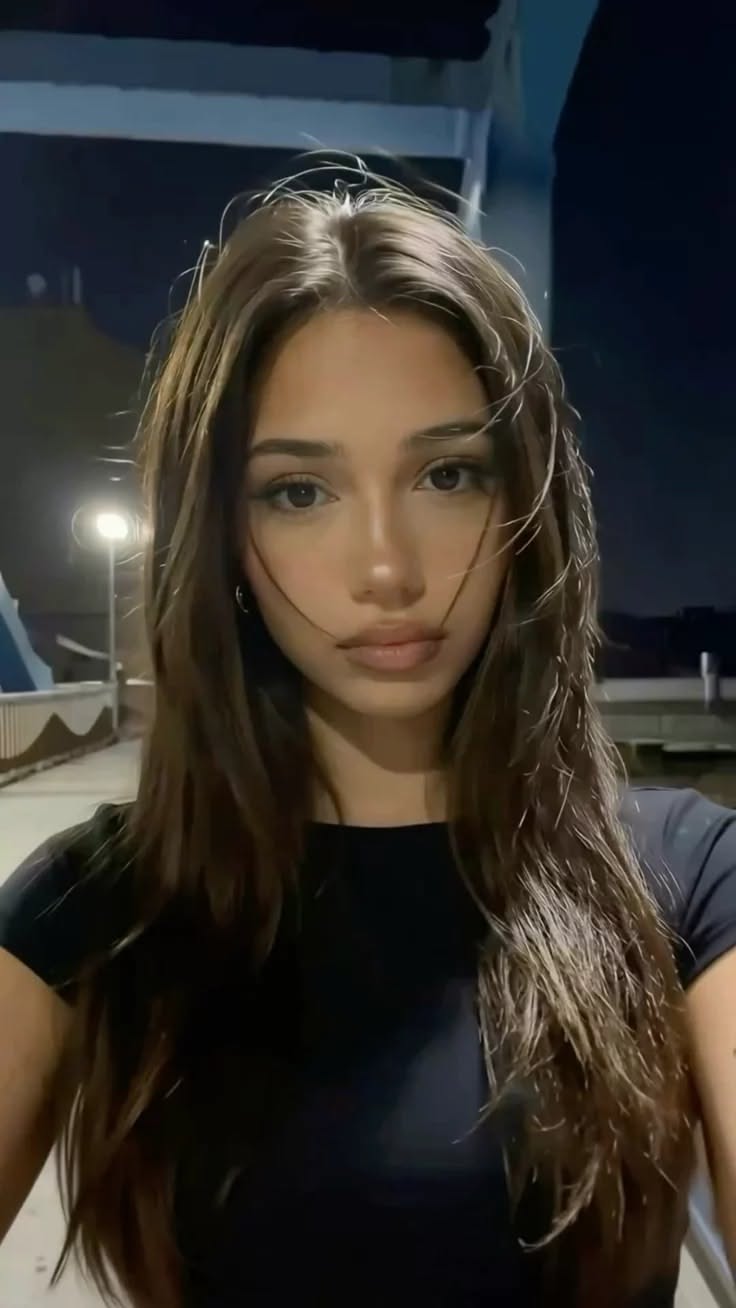 Woman with long dark hair wearing a black shirt at night outdoors