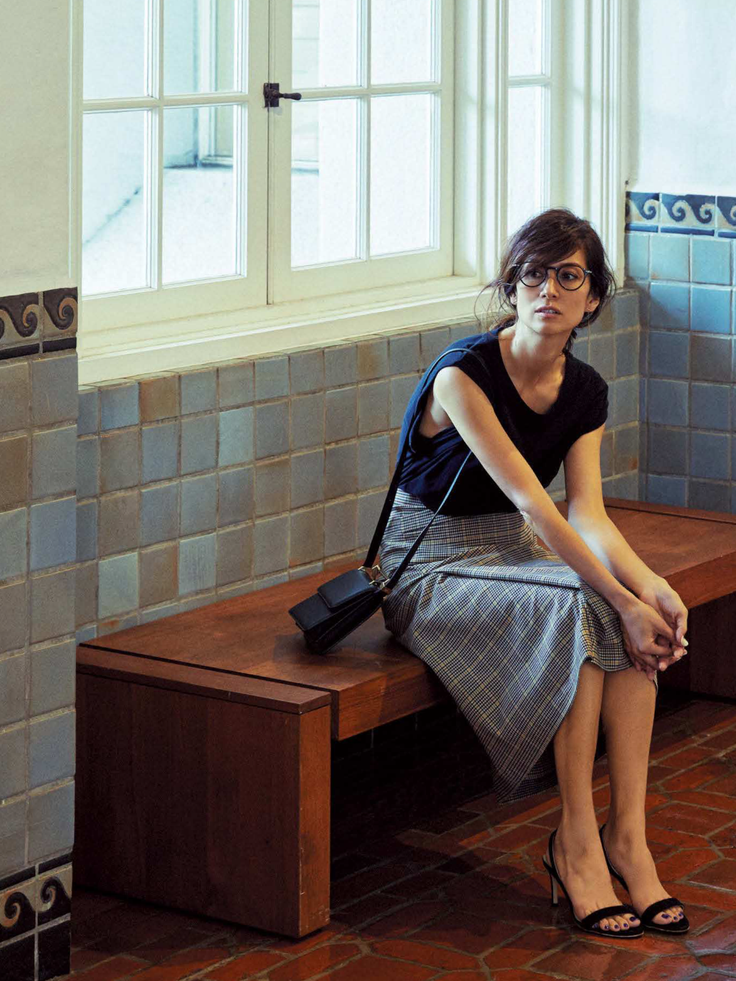 Woman with short hair and glasses sitting on a wooden bench indoors