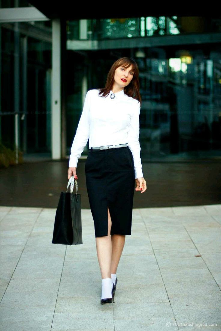 Woman in a white shirt and black skirt walking outdoors with a black handbag