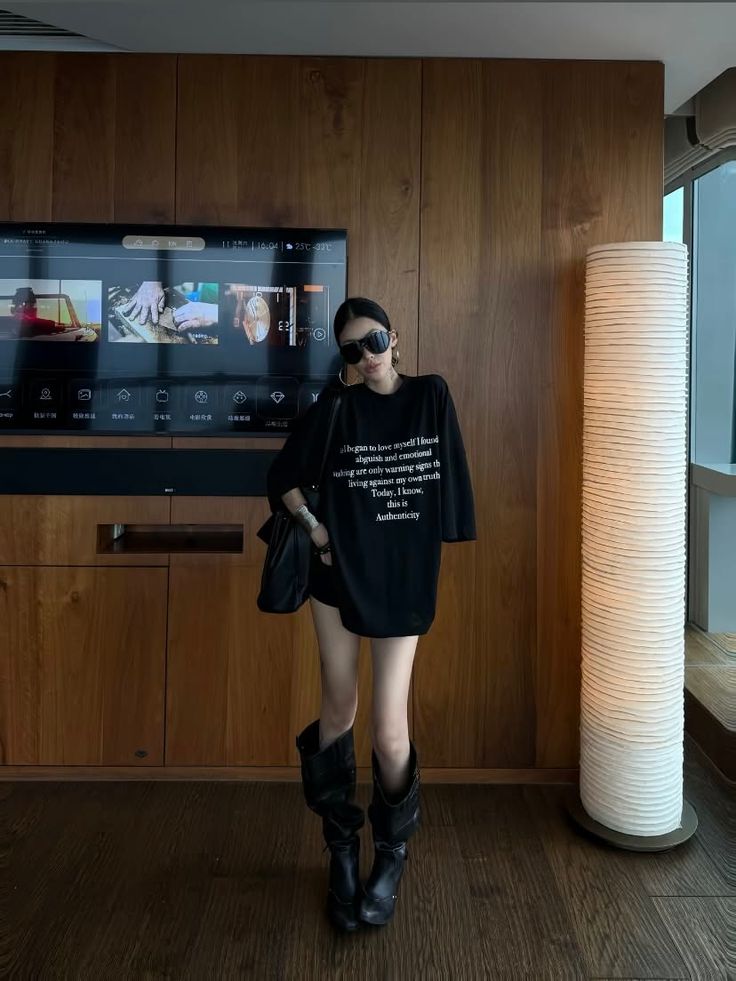 Woman in an oversized black t-shirt and boots standing indoors