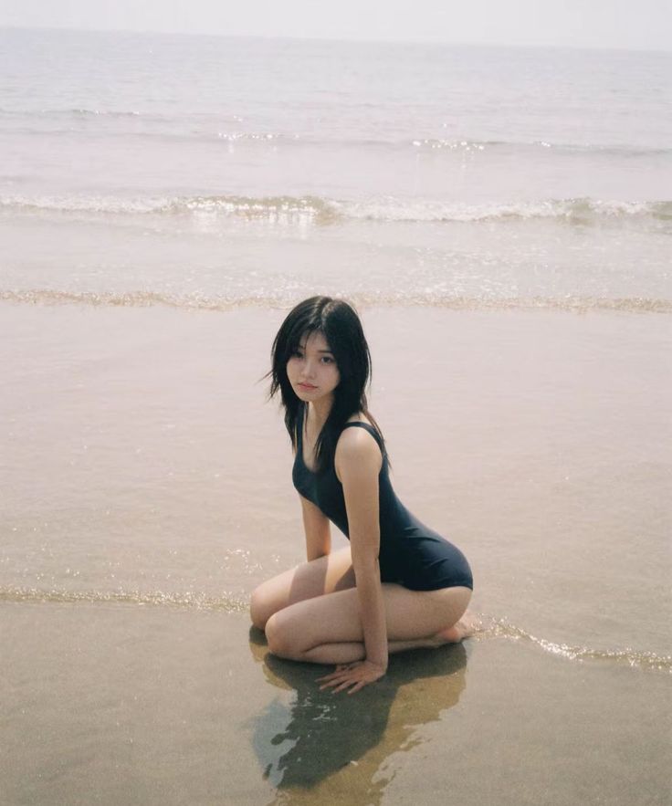 Woman in a black swimsuit kneeling on wet sand at the beach