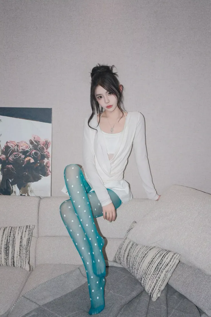 Woman with a messy bun and teal polka dot tights sitting on a sofa